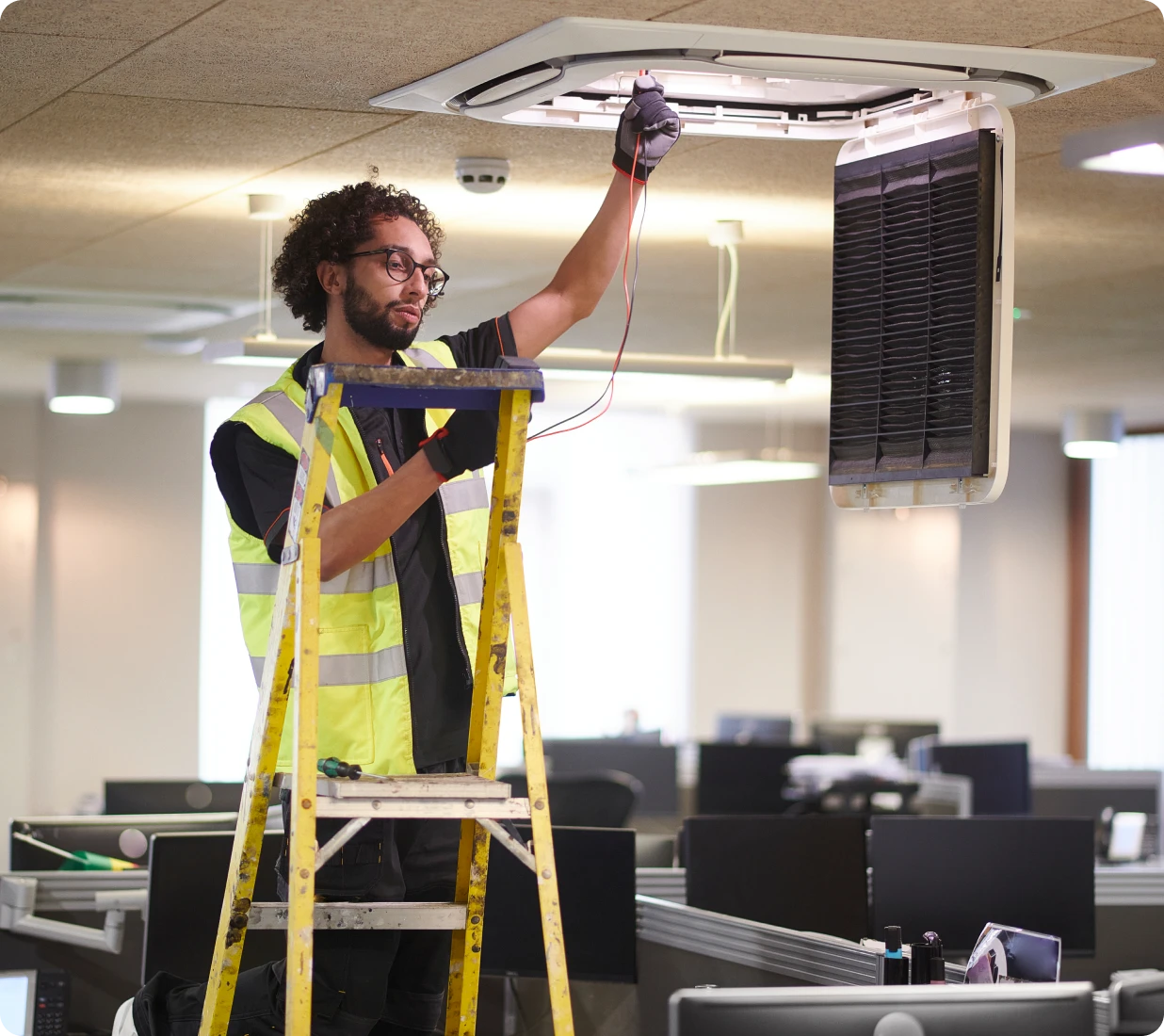 Worker on ladder fixing office air conditioner